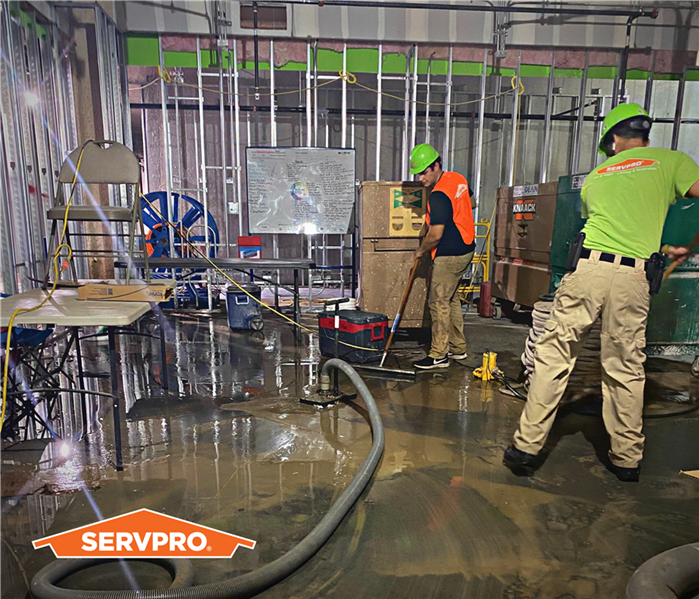 SERVPRO crew members cleaning up after a water disaster in a commercial warehouse, wearing orange vests