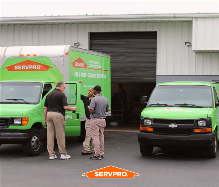 two green servpro of oviedo /wse box trucks, 3 servpro employees standing by one with the door open, front of warehouse
