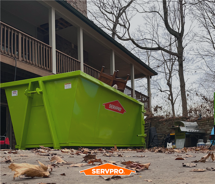 SERVPRO large green trash container in front of residential home, tossed items inside covered in mold
